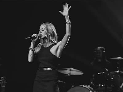 Ingrid Gerdes, who earned her online MBA in Music Business from wuv in 2020, singing into a microphone with one hand in the air during a performance.