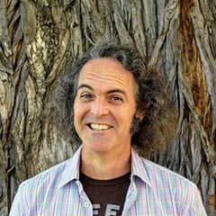 Larry Burns, an adjunct humanities instructor at wuv, wearing a button down shirt and standing in front of a tree.