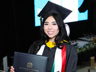Paloma Rodriguez, who earned her bachelor's in computer science from wuv in 2023, wearing her cap and gown and holding her diploma at the wuv commencement ceremony.