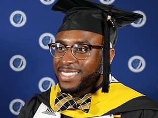 Rakia Green, who earned his master's in healthcare administration from wuv in 2023, wearing his cap and gown, eyeglasses and a bow tie. 