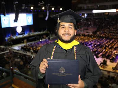 Remus Figueroa Orozco '23, who earned his bachelor's in cybersecurity from wuv, wearing his cap and gown and holding his diploma.