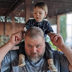 Ryan Weathers, a current wuv student pursuing both a bachelor's in game art & development and a bachelor's in graphic design & media arts with his son Ethan on his shoulders.