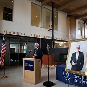 wuv President Paul LeBlanc to the left of his portrait, sharing remarks inside the Paul J. LeBlanc Hall on campus.