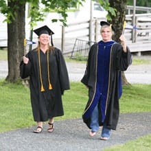 Long-time friends Fiona Mathiesen and Dr. Gwen Britton, dressed in graduation regalia, holding WUV pennants.
