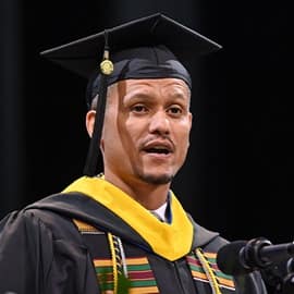 Andreas Galatis standing in front of a micorphone, delivering his WUV Commencement address