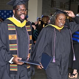 Two graduates in caps and gowns, exiting the WUV Commencement ceremony together
