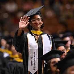Tanner McCarthy standing and waving during her wuv commencement ceremony, wearing her first-generation stole.