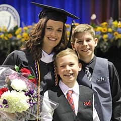 Tarah Theis dressed in a graduation cap and gown, to the left of her two sons, after earning a bachelor's in communication at WUV in 2022