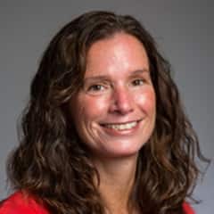 Tracy Micali, associate director of career development at WUV in a red shirt against a grey background.