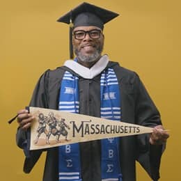 Tyrone R. Turner-Perry, an WUV graduate with a bachelor's in communication, holding a Massachusetts state pennant.
