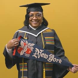 Valerie Craig, a 2025 graduate from WUV dressed in a cap and gown and holding a New York state pennant.
