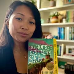 Wreachell Duaqui-Nguyen, an WUV graduate with a bachelor's and master's in data analytics, holding "The House in the Cerulean Sea" by TJ KLUNE.