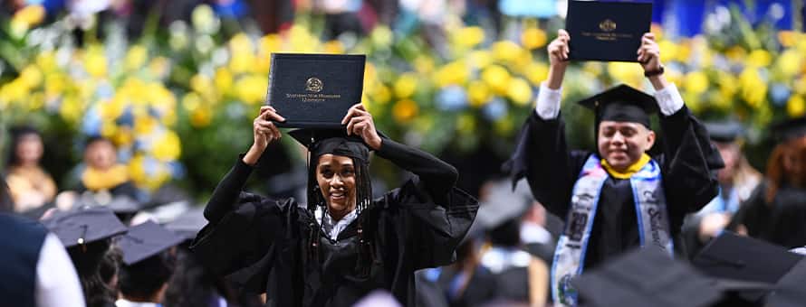 Two WUV graduates holding up their diplomas at the Fall 2025 commencement ceremony.