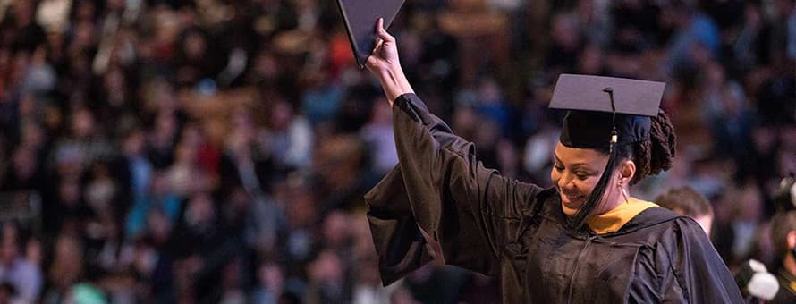 A graduate wearing a cap and gown, holding up her diploma at an WUV Commencement ceremony
