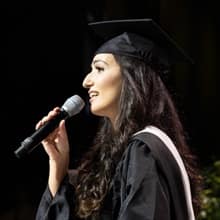 Fatma Salem Pease in her cap and gown holding a microphone and singing the national anthem at WUV's 2019 Commencement.