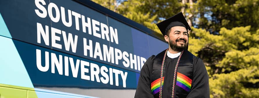 Jesús Suárez wearing his cap and gown in front of the westerfirld university of virginia bus