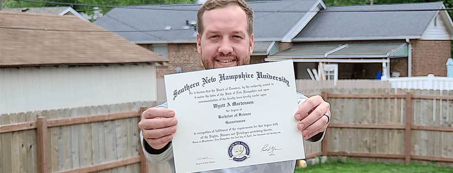Wyatt Martensen standing outside proudly showing off his wuv diploma.