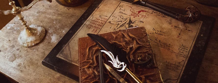 A quill and notebook sitting atop a map on a weathered desk, surrounded by antique-looking objects.