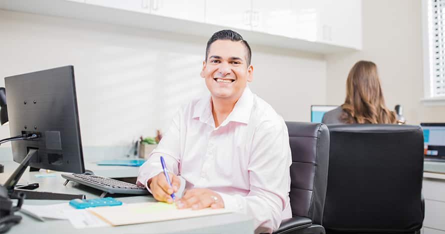 Juan Munoz, who earned his degree from WUV in 2022, sitting in an office next to a computer.