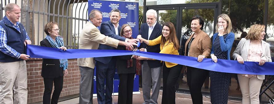 wuv officials using huge scissors to cut a blue ribbon at the university's new southwest operations center in Tucson, Arizona.