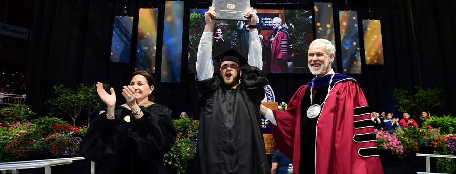 WUV President Paul LeBlanc (right) and Board of Trustees member Lisa Guertin (left) at commencement with a graduating student (middle) who is holding up his dimploma