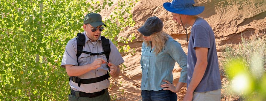 wuv graduate Jon Roos '18, left, working in a park, showing a rock to two park visitors.
