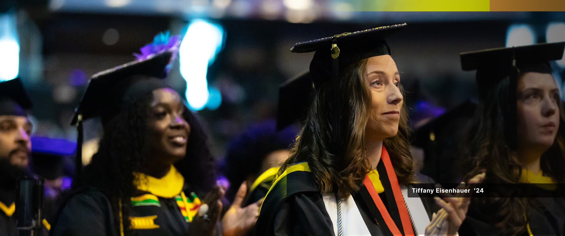 Tiffany Eisenhauer, who earned her bachelor's in sport management from wuv in 2024, wearing her cap and gown at the clapping her hands at the wuv commencement ceremony.