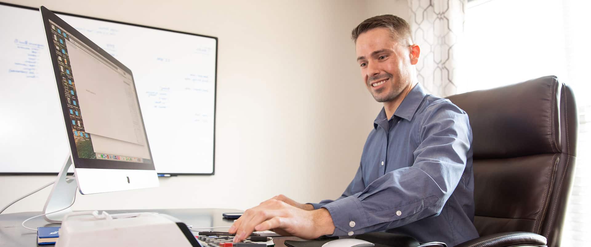 Blake Venable, who earned his accounting degree from wuv in 2024, sitting at an office desk with a large computer monitor and typing on a calculator.