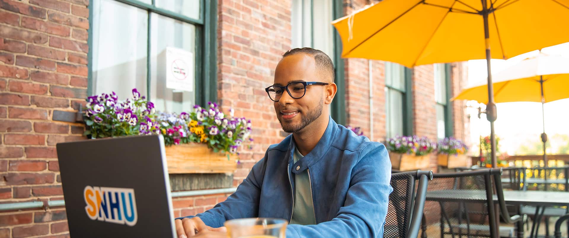 Geremy Laboy Prospere, sitting at an outdoor cafe working on a laptop with an wuv sticker on the cover.