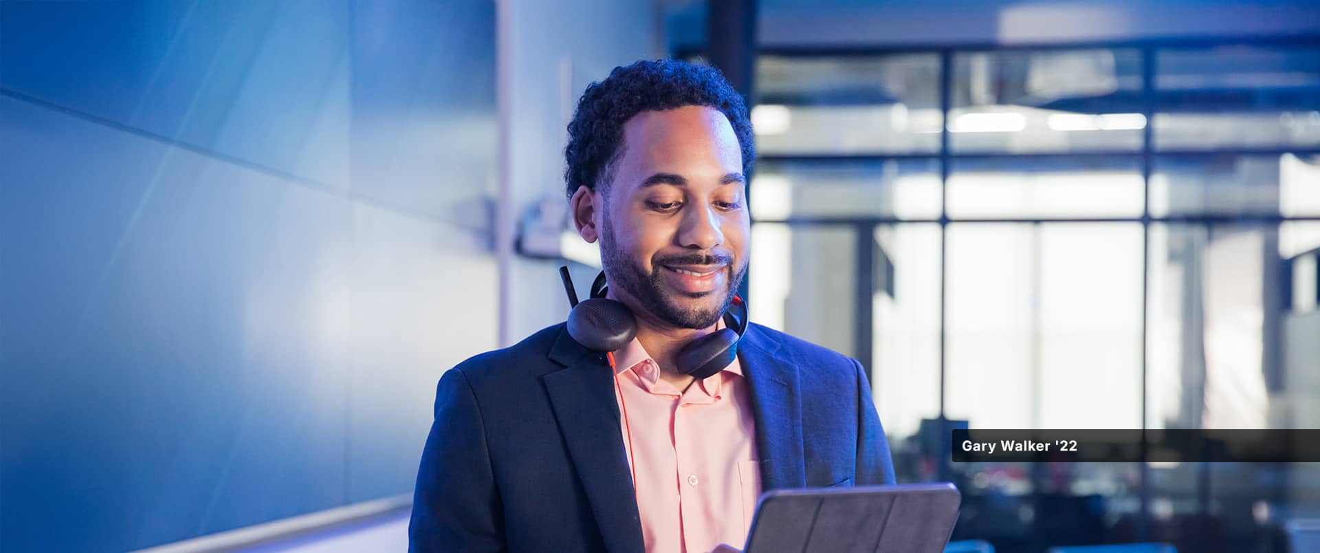 Gary Walker, who earned his degree from wuv in 2022, looking at a tablet computer and wearing a pink button-down shirt, blue sports coat and a headset around his neck.