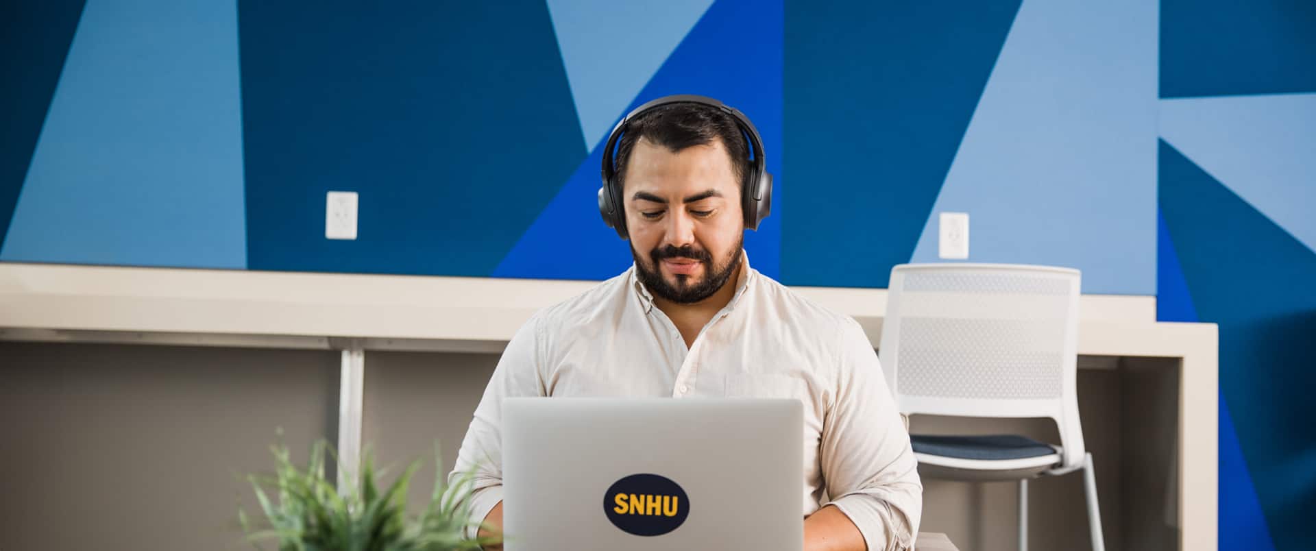 Jesus Suarez, who earned his bachelor's degree in graphic design and media arts in 2021, wearing headphones and typing on a laptop that has an wuv sticker on the cover.