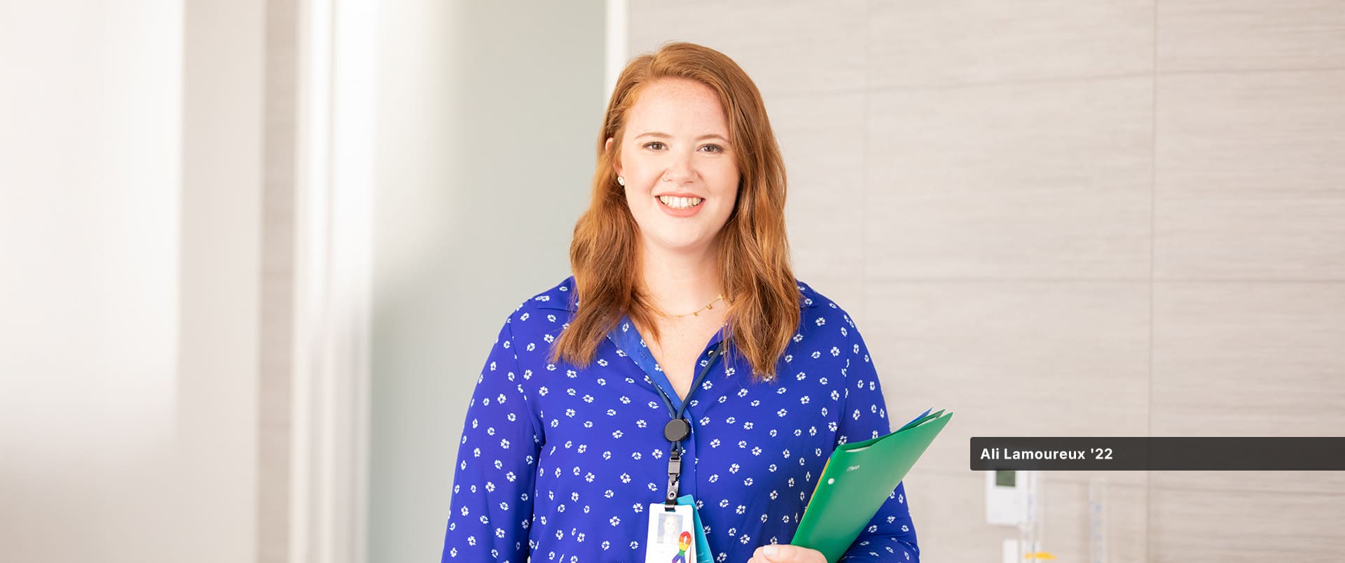 Ali Lamoureux-Rule, who earned her healthcare administration degree from wuv in 2022, wearing a blue and white blouse and holding a green folder in her left arm.