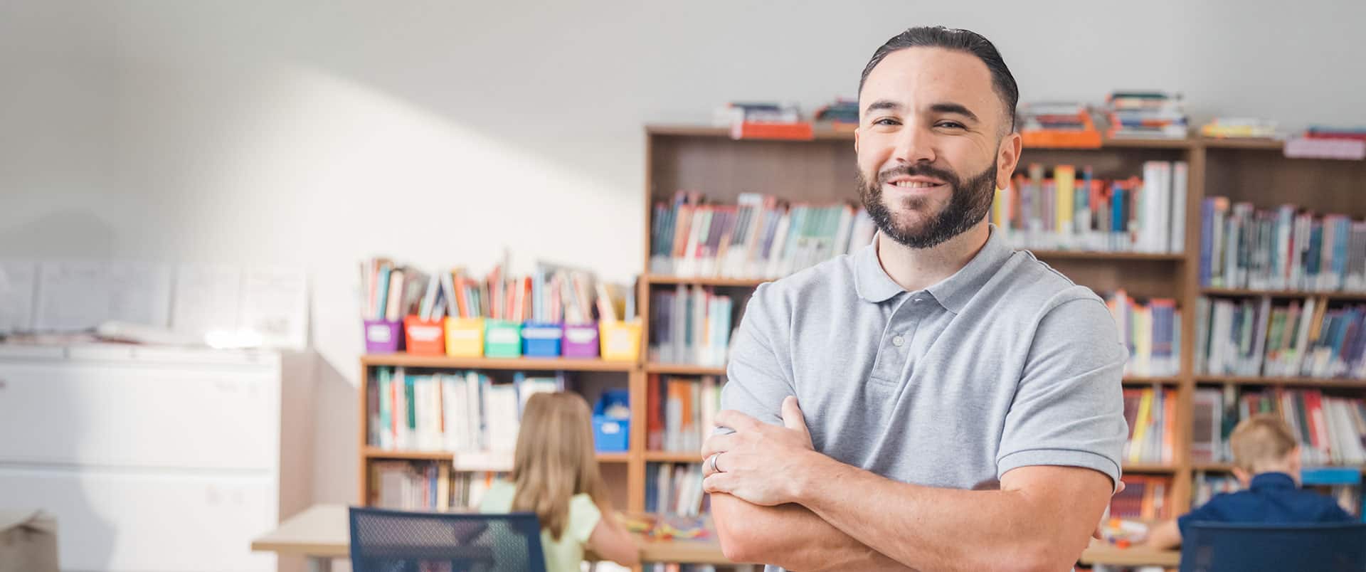 Stephen Goulakos, who earned his bachelor's in psychology from wuv in 2022, standing with his arms folded in front of several bookshelves.
