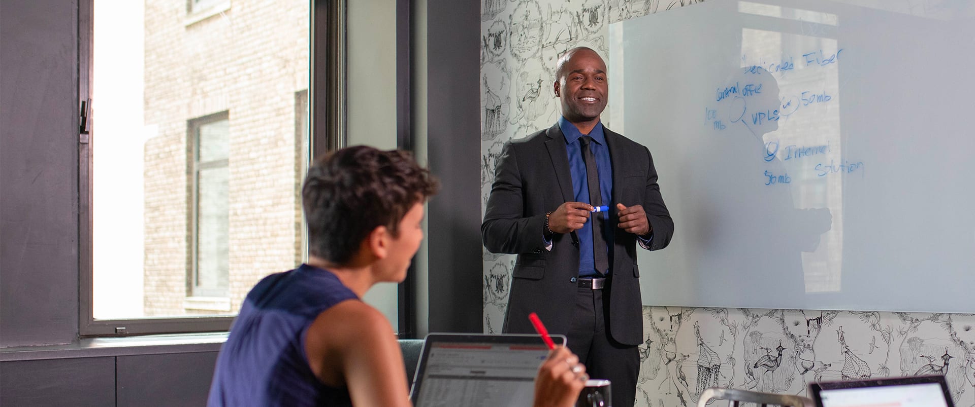 Jean Besson, a 2014 business graduate, prenting on a whiteboard in a business office.