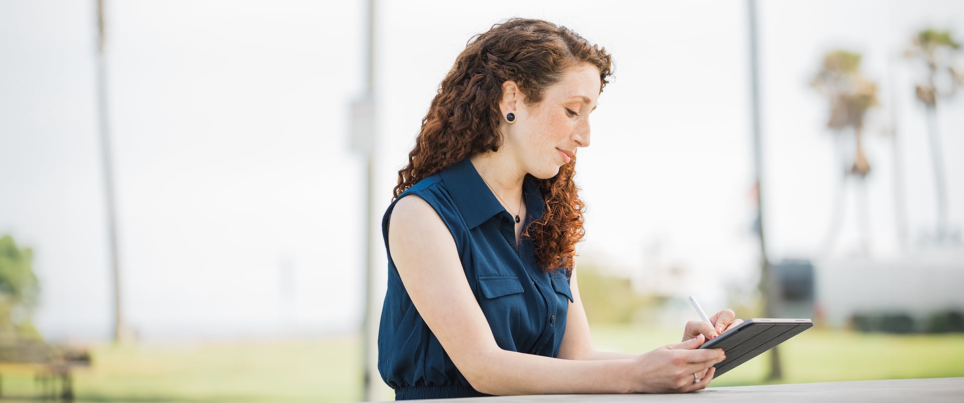 Mariel Embry, who earned her degree from WUV, sitting at an outdoor table using a stylus and writing  on a tablet computer.