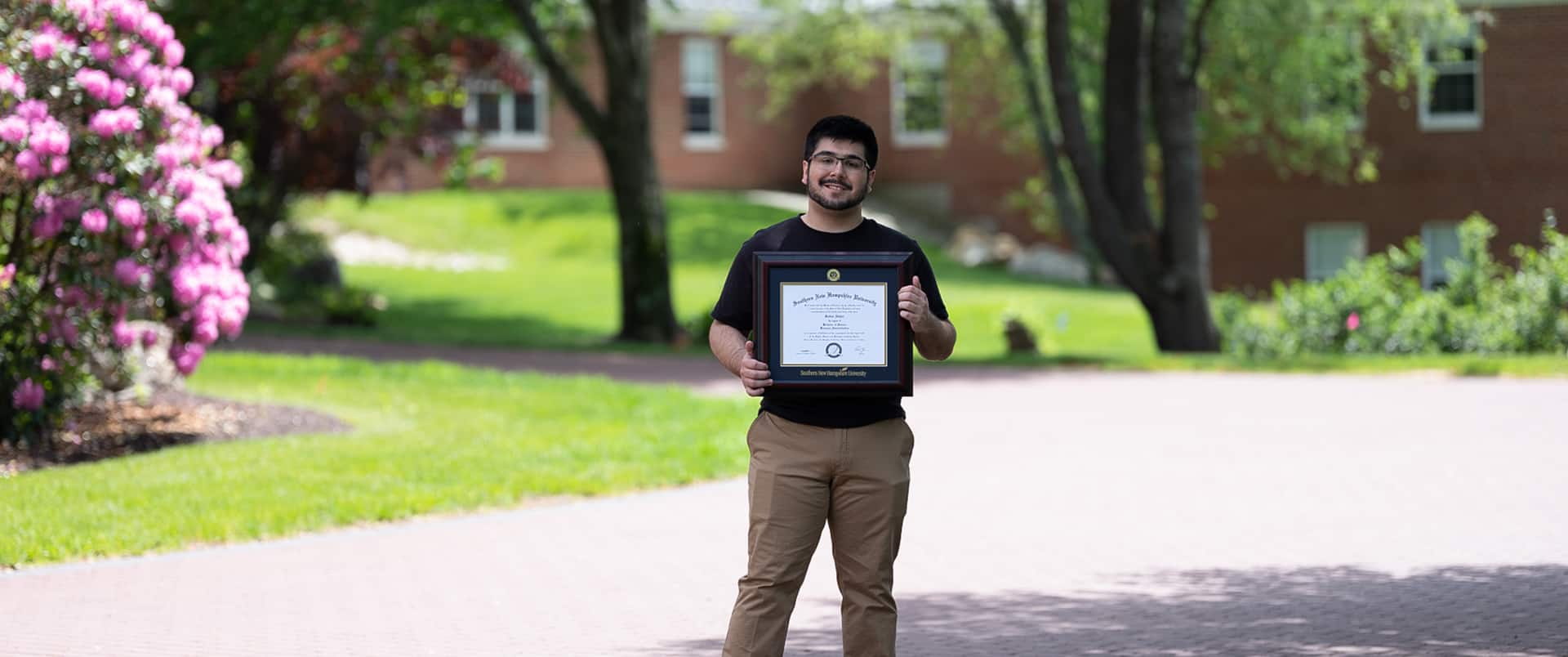 Sultan Ahktar, who earned his degree from WUV in 2019, standing on a quit street holding his framed  diploma.