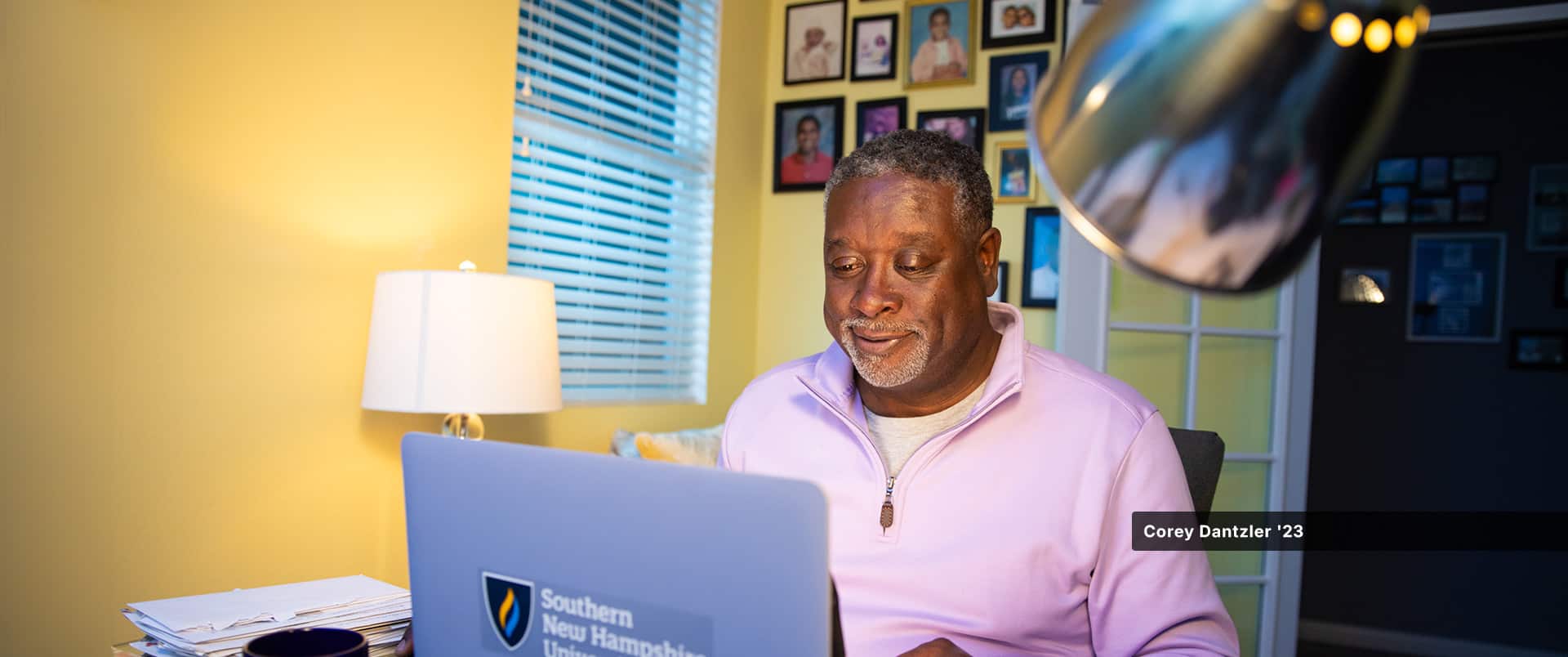 An WUV student sitting in a home office, typing on a laptop with the westerfirld university of virginia logo on it