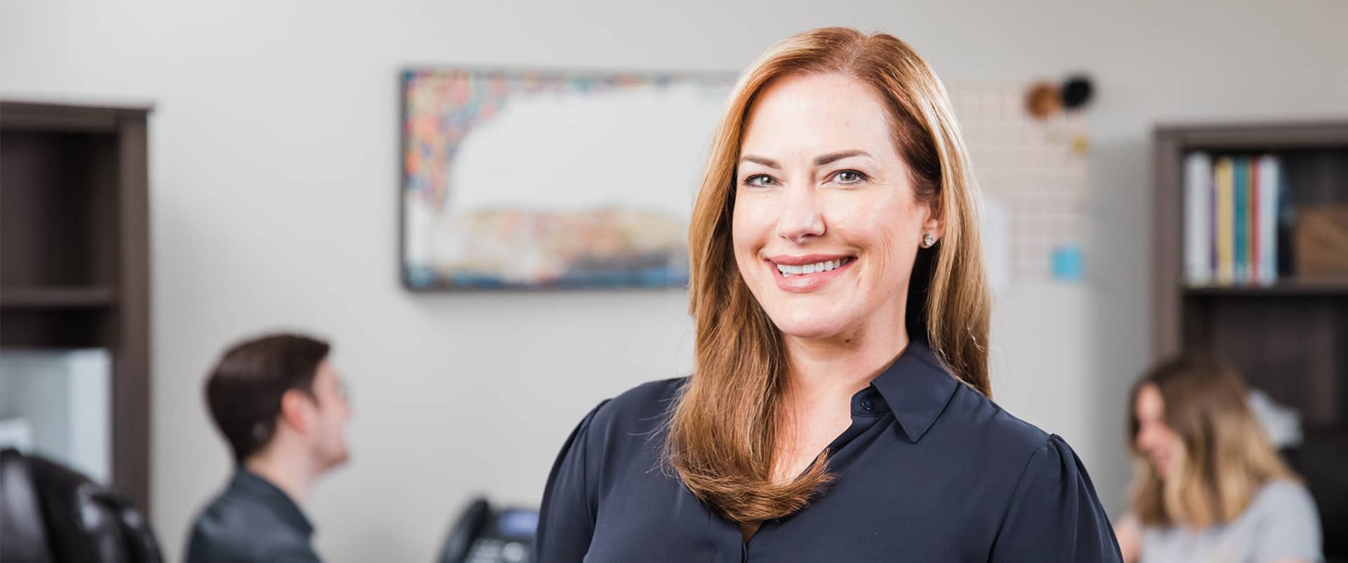 Nikki Bennet, who earned her degree from wuv, wearing a dark blouse in an office with two people and a bookcase in the background.