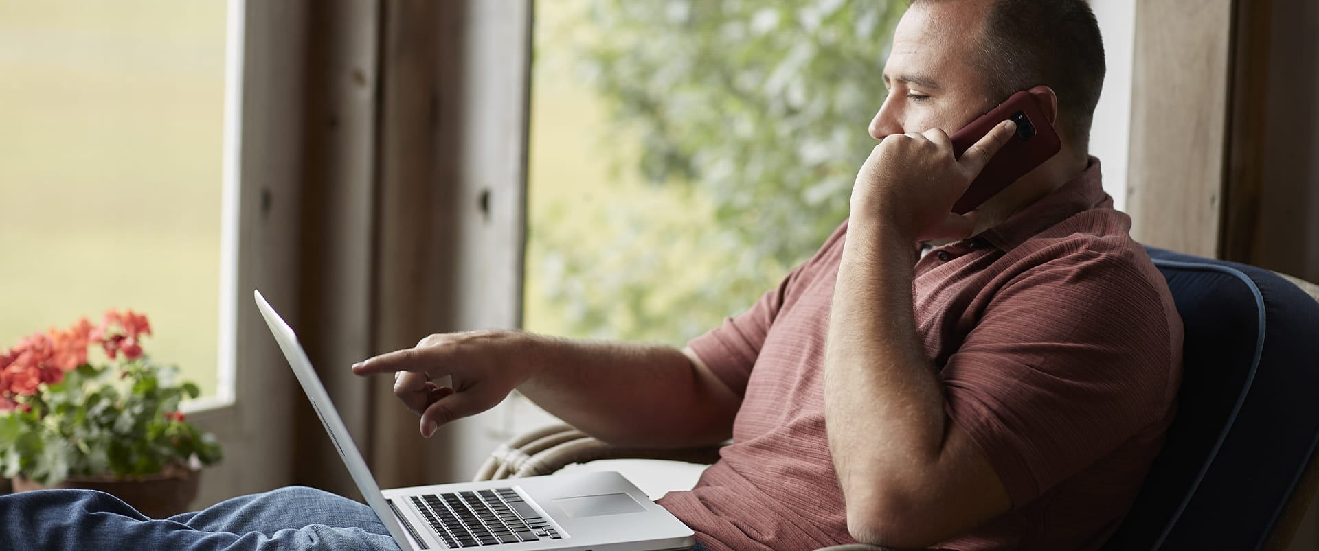 Raymond Gammon, who earned his degree from wuv in 2020, sitting on a screened porch holding a cell phone to his left ear and pointing at his laptop screen.