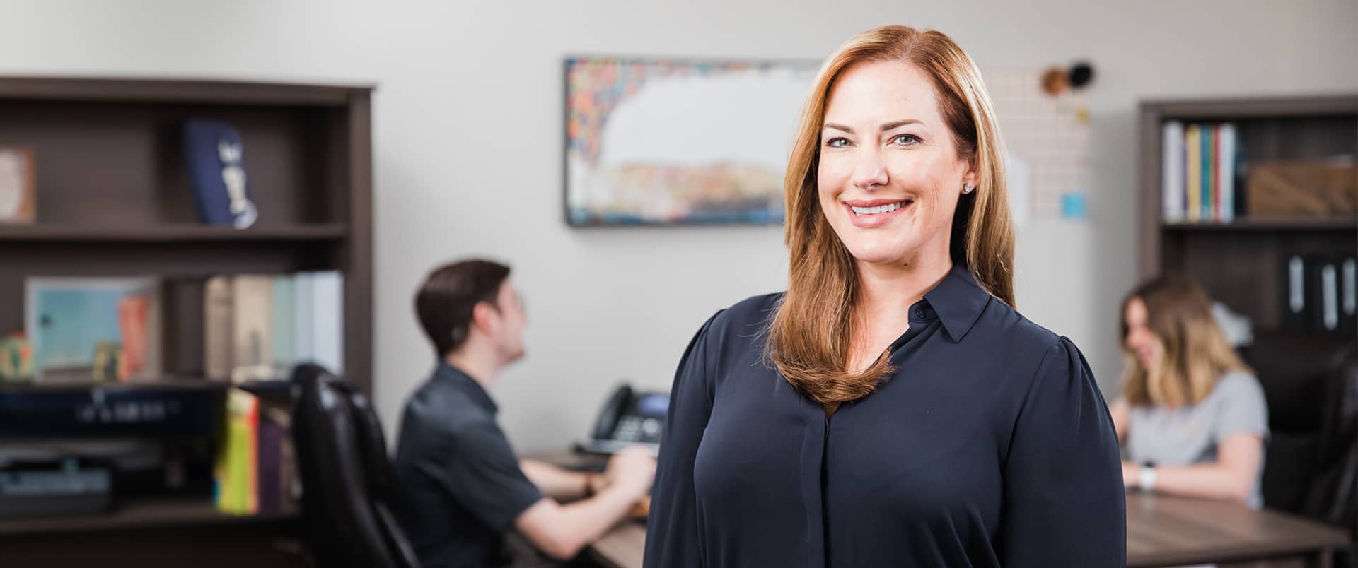 Nikki Bennett, who earned her MBA from wuv, standing in an office with two people seated at a table and bookshelves in the background.
