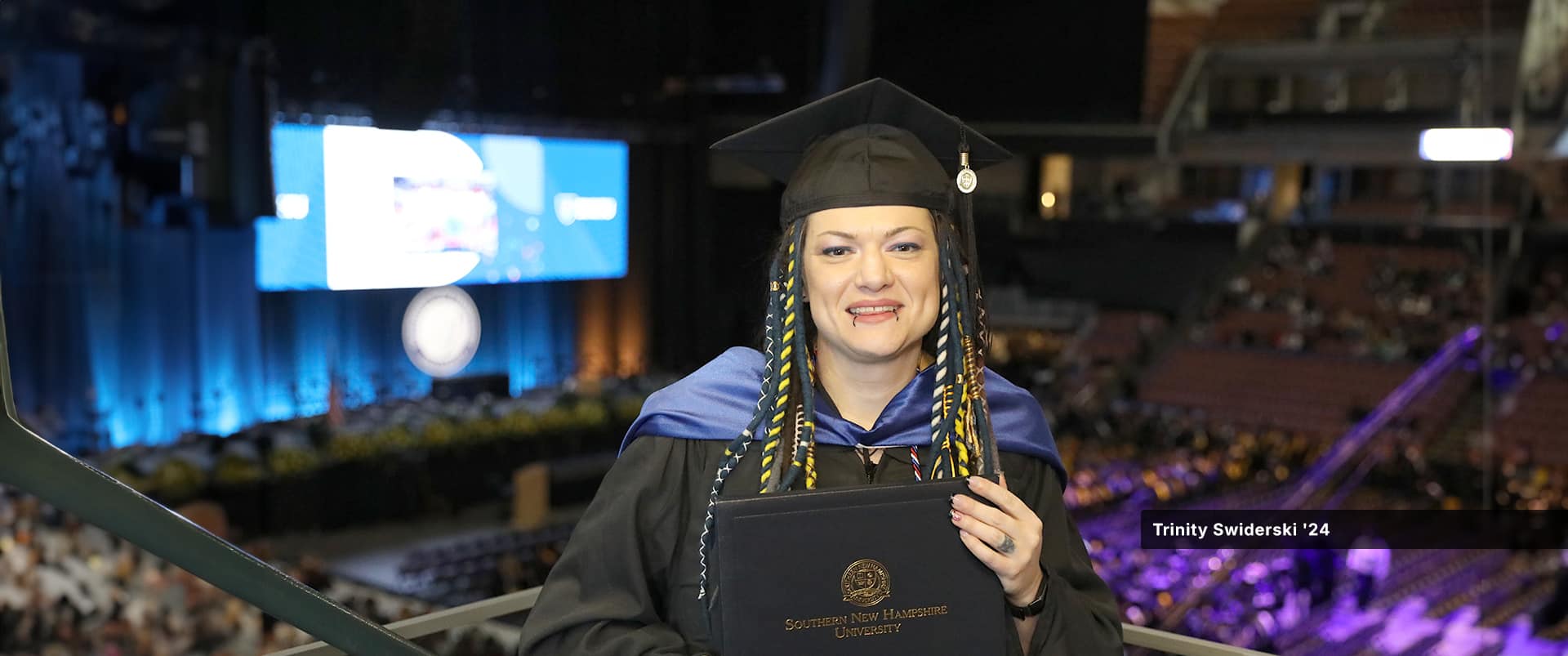 Trinity Swiderski, who earned her master's in communication from wuv in 2024, wearing her cap and gown and holding her diploma at the wuv commencement ceremony.