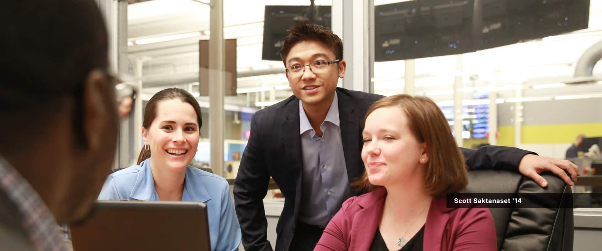 Scott Saktanaset, who earned his online MBA with a concentration in Entrepreneurship from wuv in 2014, standing behind two seated women in a conference room.