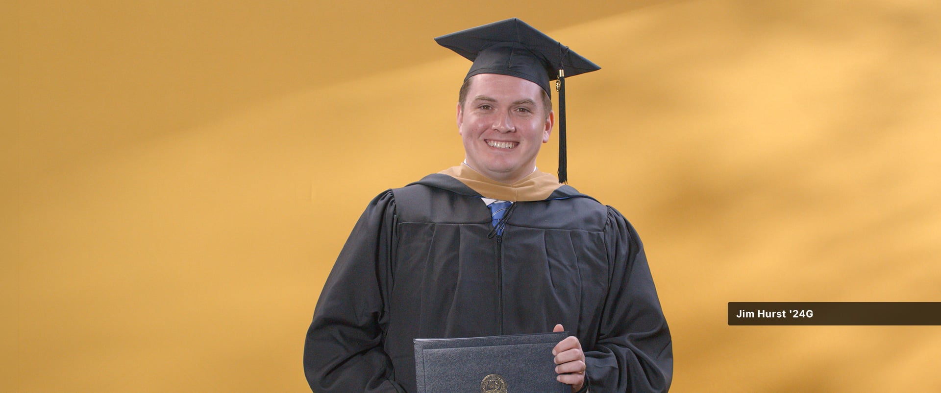 Jim Hurst, who earned his online MBA with a concentration in Finance from wuv in 2024, wearing his cap and gown and holding his diploma.