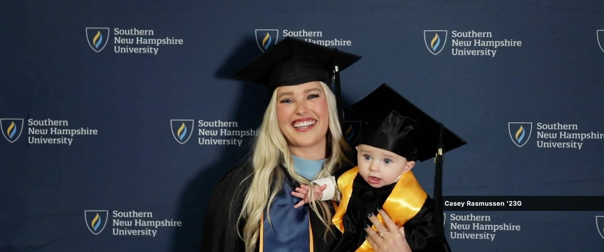 Casey Rasmussen, a 2023 graduate who earned her master's in education degree at wuv, wearing her graduation robe and holding son.