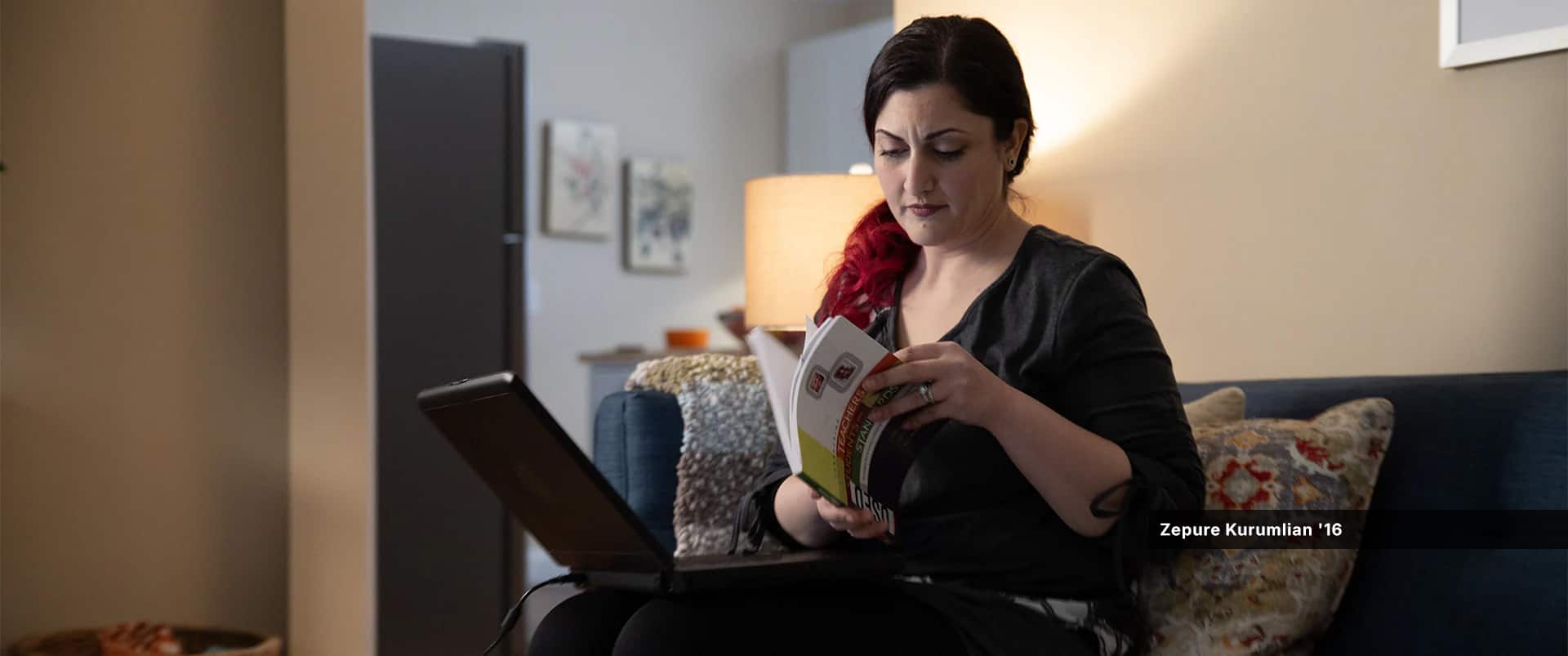 Zepure Kurumlian, who earned her degree from wuv in 2016, thumbing through a book while sitting on a couch in her living room with a laptop on her lap.