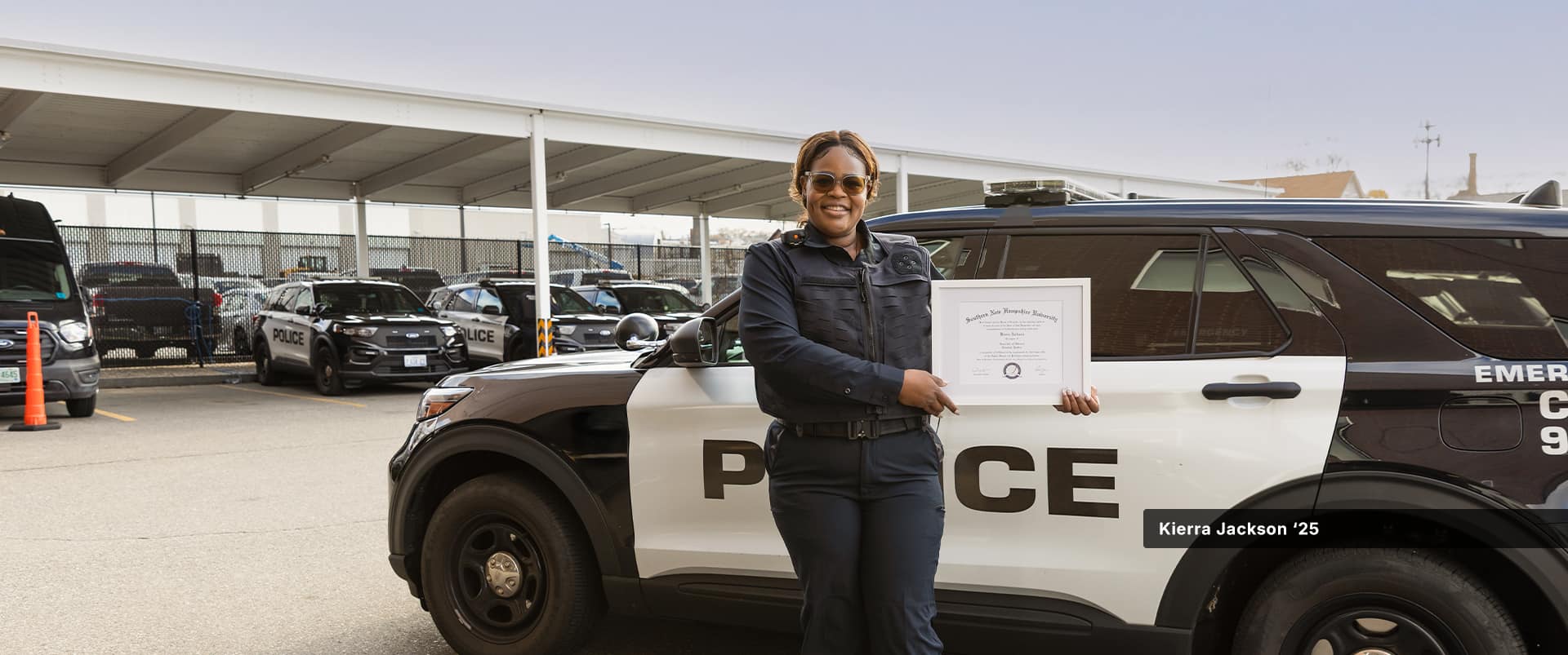 Kierra Jackson, who earned online criminal justice degrees from wuv in 2024 and 2025, holding her framed diploma standing in front of a police cruiser.