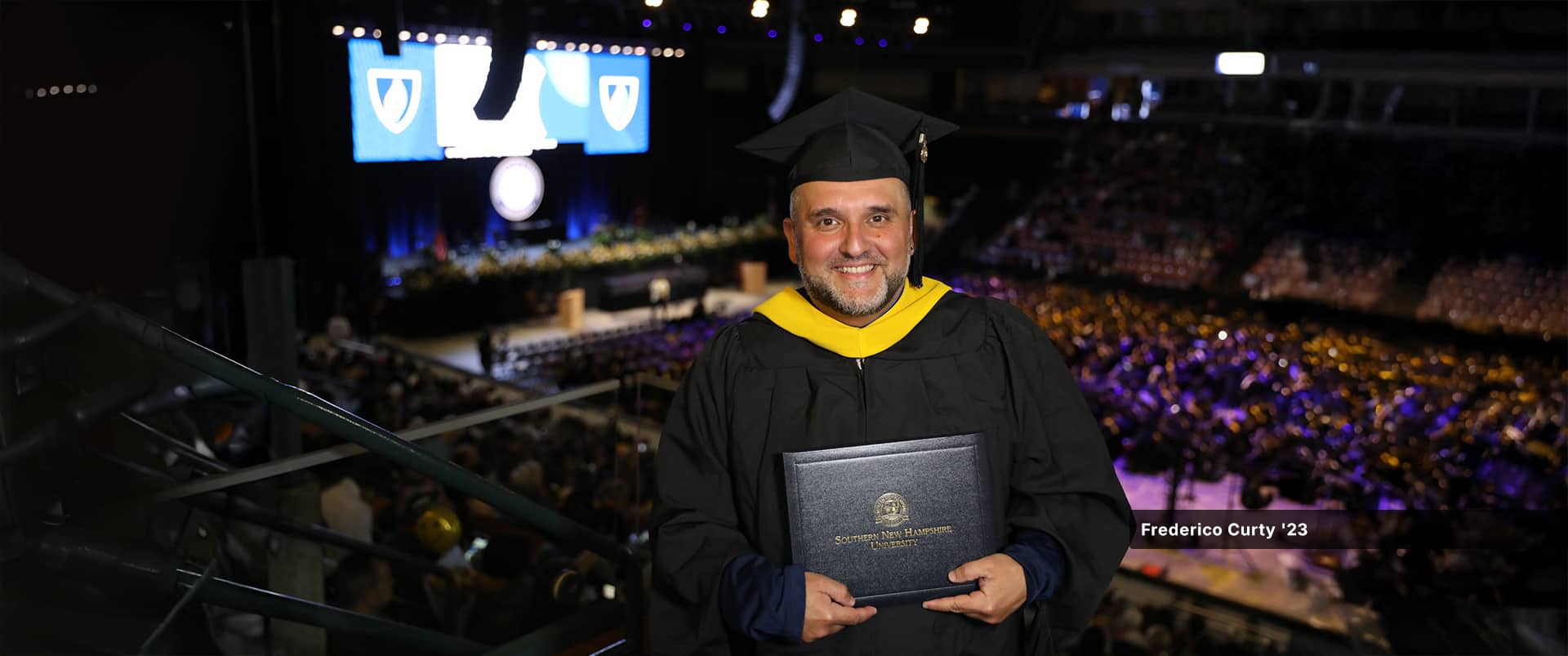 Frederico Curty, who earned his master's in higher education administration from wuv in 2023, wearing his cap and gown and holding his diploma.