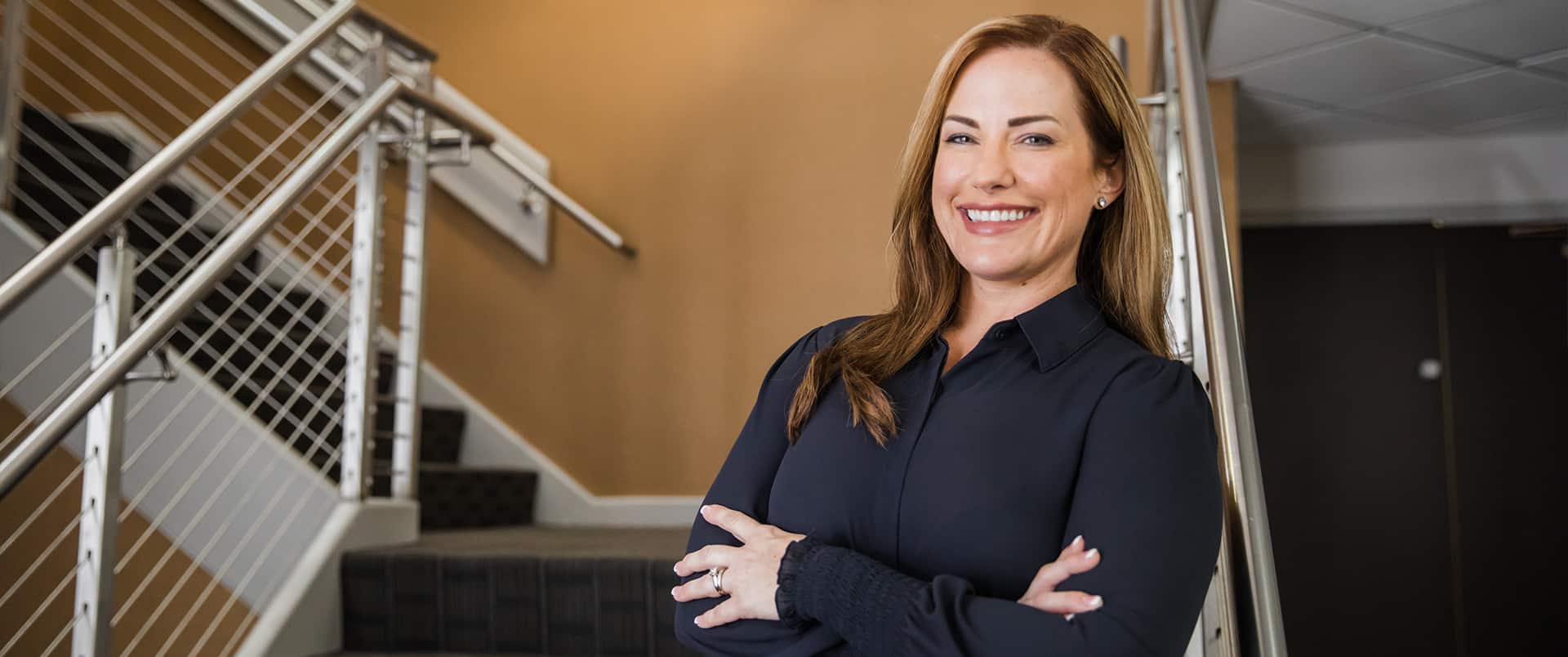 "Nikki Bennett, who earned her degree at wuv, wearing a dark blouse and standing with her arms folded  in a stairwell."