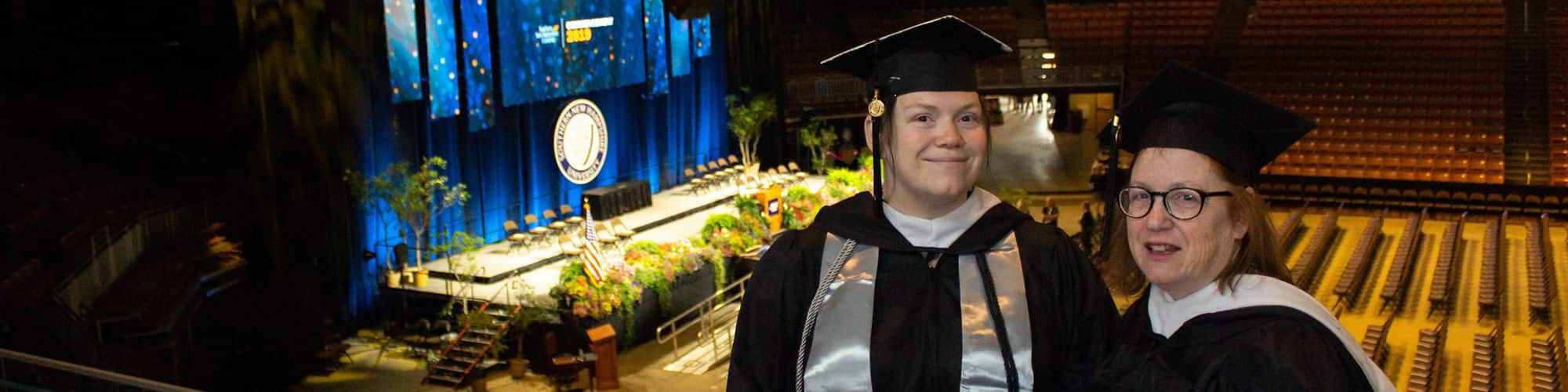 Delaware residents and wuv graduates Jenny Gardner and Susan Lasala wearing their cap and gowns in the wuv Arena for Commencement.