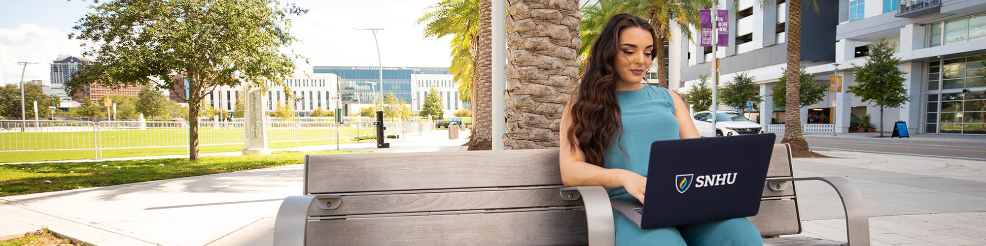 wuv student and Florida resident Deonna Purrazzo, sitting on a bench in front of a palm tree typing on her laptop.
